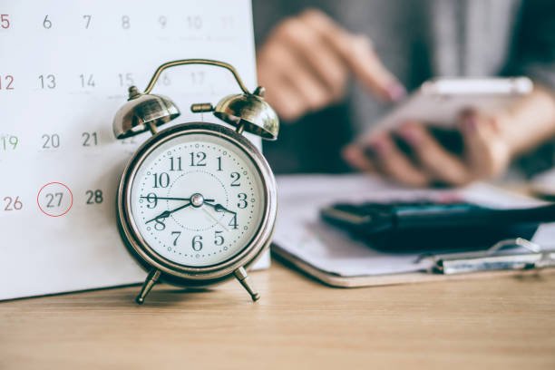 due date calendar and alarm clock with blur business woman hand calculating  monthly expenses during tax season.