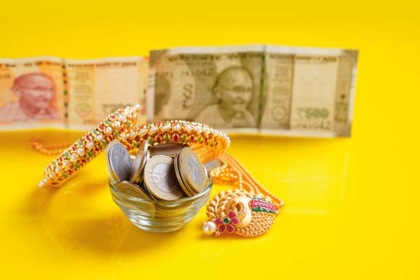 Gold bangles and indian rupees coins in bowl on yellow background